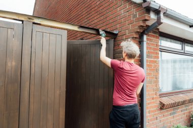 Genç bir işçi fırçayla ahşap bir çit kapısı boyuyor. DIY, kendin yap. Ev tadilatı. Ev tadilatı ve yenilenme. Seçici odak, boşluğu kopyala