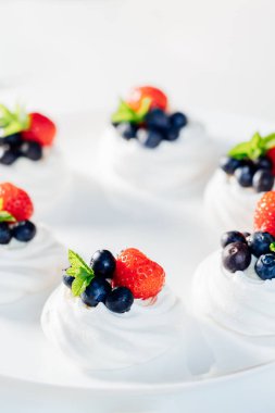 Beyaz tabakta naneyle süslenmiş taze kremalı, çilekli ve yaban mersinli Pavlova pastası. Lezzetli hafif tatlılar için reçeteler. Şekerleme kafe menüsü. Seçici odak.