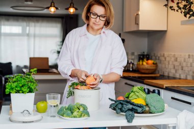 Mutfak atıklarını gübrelemek, evde geri dönüşüm yapmak. Tatlı patatesleri temizleyen, artıkları çöpe atan, mutfaktaki gübre kutusunu karıştıran bir kadın. Çevreye duyarlı, ekoloji.