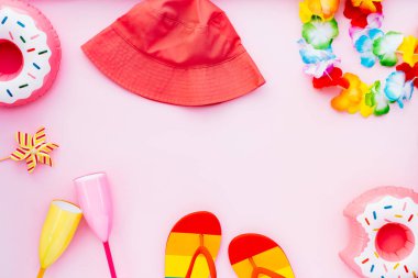 Renkli havuz partisi eşyaları, kokteyl bardakları, şişirilebilir içecek tutacakları, parmak arası terlikler, pembe arka planda kova şapka ve çiçek kolyeleri içeren düz yaz titreşimleri konsepti.