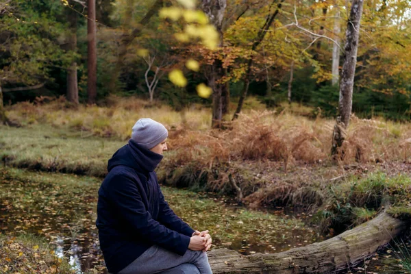 Young Man Warm Clothes Sitting Fallen Tree River Looking Forest — Fotografia de Stock