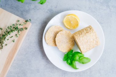 Top view raw Tempeh or Tempeh, made of fermented soybean seeds. Tempeh Slices on plate with herbs. Soya protein. Plant based meat concept. Healthy Cooking and eating. Go vegan. Flat Lay, copy space.