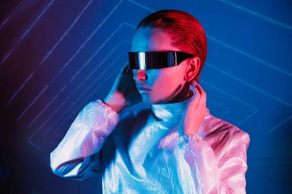 Neon portrait of woman, dressed in futuristic holographic clothes and glasses. Portrait of a cyberpunk girl. Neon blue and pink light. Virtual reality glasses. Fashion, futuristic generation concept