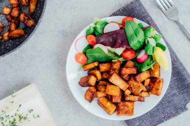 Top view healthy salad with cherry tomato, beetroot straws, spinash and lettuce leaves, portion of roasted tempeh, made of fermented soy bean on plate. Plant based protein. Healthy eating. Go vegan.