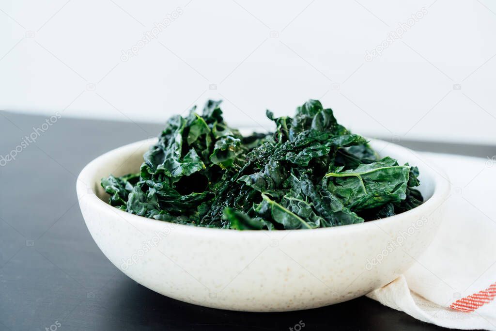 Teared curly green kale leaves in the plate with seasonings and olive oil on the kitchen table. Ingredients for kale chips or healthy salad meal. Healthy eating, dieting lifestyle. Selective focus
