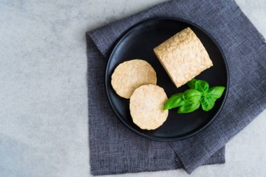 Top view raw Tempeh or Tempeh, made of fermented soybean seeds. Tempeh Slices on plate with herbs. Soya protein. Plant based meat concept. Healthy Cooking and eating. Go vegan. Flat Lay, copy space.