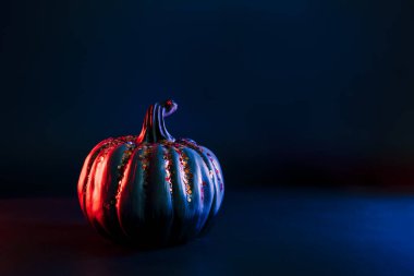 Decorative pumpkin with orange sparkles in neon red and blue light on the dark. Halloween decor and background with copy space. Selective focus.