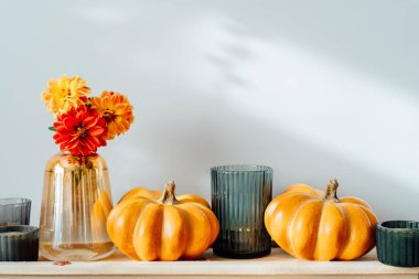 Autumn, fall cozy composition. Orange pumpkins, candles, dahlia flowers in vase on the wooden tray on the table with white wall background. Scandinavian minimalist hygge home decor. Selective focus.