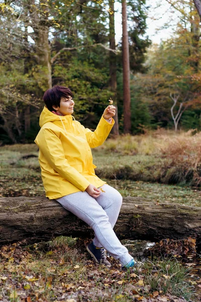 Woman Bright Yellow Raincoat Sitting Fallen Tree Fallen Leaves Enjoying — Foto de Stock