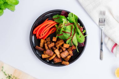 Top view healthy green salad, sliced pepper and and portion of roasted tempeh, made of fermented soy bean on the plate. Plant based protein. Healthy cooking and eating. Go vegan. Flatlay.