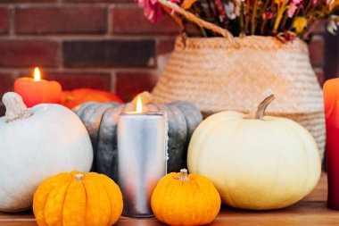 Festive composition for autumn holidays. Burning candle, various pumpkins and flowers bouquet in the wicker basket on brik wall background. Thanksgiving or Halloween. Fall Harvesting. Selective focus.