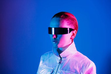 Neon portrait of woman, dressed in futuristic holographic clothes and glasses. Portrait of a cyberpunk girl. Neon blue and pink light. Virtual reality glasses. Fashion, futuristic generation concept