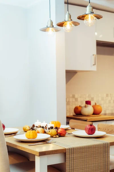 Fall table setting for celebration Thanksgiving day family party. Autumn composition with candles, fruits, nuts and cones. Plates with pumpkins and pomegranate. Natural autumn decor. Selective focus.