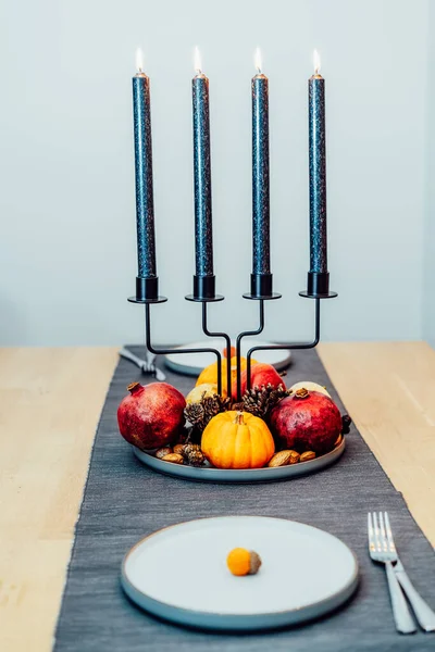 Fall table setting for celebration Thanksgiving day for two. Autumn composition with candles, pumpkins ,pomegranate and cones. Natural autumn decor. Vertical card. Selective focus.