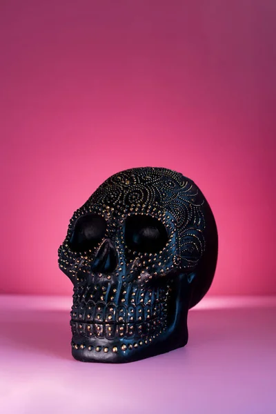 Black human skull decorated with golden points pattern on the pink background. Halloween decor concept. Vertical card. Selective focus, copy space