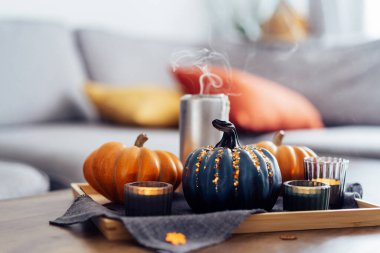 Hygge ev dekorasyonu için sonbahar kompozisyonu. Turuncu ve gri balkabakları. Oturma odasındaki sehpada gri bir peçeteyle tepside mumları söndürüyorlar. Seçici odaklanma. Boşluğu kopyala.