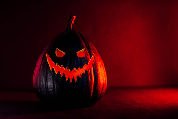Жуткая черная тыква Хэллоуина, Джек О Фонарь, с освещенным злым лицом и глазами на кровавом красном и черном фоне с копировальным пространством. Счастливый Хэллоуин. Праздничная открытка.