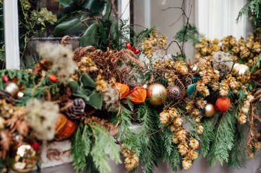 Taze yeşillikler, kırmızı böğürtlenler, koniler ve çiçeklerle süslenmiş kış tatili penceresini kapat. Doğal malzemelerden yapılmış dış dekorasyon. Noel şenliği şehri. Seçici odak