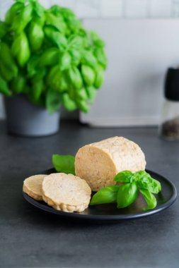 Raw Tempeh or Tempe, made of fermented soybean seeds on kitchen table. Tempeh Slices on the plate. Soya protein. Plant based meat. Healthy eating. Go vegan. Vertical card. Selective focus, copy space.