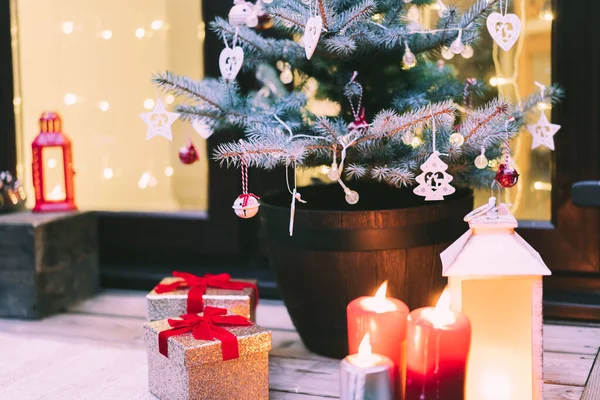 圣诞节庆祝活动 在户外的房子门廊上 有一棵自然盆栽的冷杉圣诞树 附有礼品盒 灯笼和烛光 背景是花环灯 圣诞节假期 有选择的重点 — 图库照片