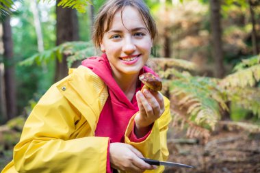 Elinde gülümseyen genç bir kadının portresi sonbahar ormanında mantar topladı. Seçme mevsimi, boş zaman ve insan konsepti. Seçici odak.