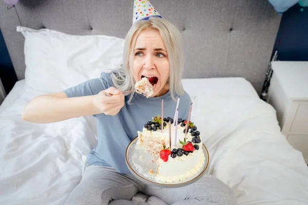 Smutna Zdenerwowana Kobieta Piżamie Imprezowa Czapka Jedząca Łyżką Tort Urodzinowy — Zdjęcie stockowe
