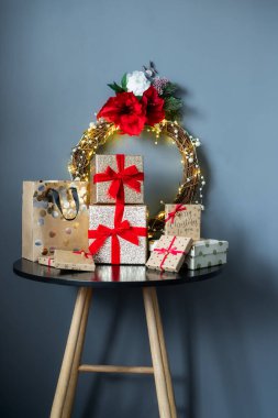 Siyah masanın üzerinde çeşitli Noel hediye kutuları ve arka planında zarif bir Noel çelengi var. Altın kutular ve kırmızı kurdelelerle dolu lüks hediyeler. Şenlik konsepti. Seçici odak