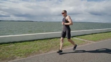 Profesyonel koşucu göl kenarındaki bir yolda koşar, atlet güneşli bir günde koşar, triatlon yarışmalarından önce koşar..
