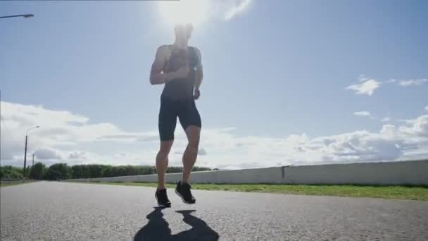 Corredor profesional corre en una carretera cerca del lago, atleta entrena en un día soleado, corriendo antes de las competiciones de triatlón. — Vídeos de Stock