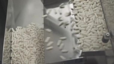 İlaç ve ilaç üretimi, çok sayıda hareket halindeki kapsül, taşıyıcıda beyaz tabletler, üretim hattında ilaçlar.