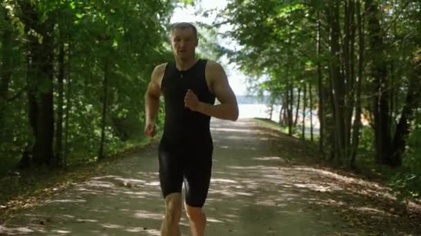 Corsa mattutina, corridore professionista corre su una strada forestale, allenamenti di atleta in un ambiente naturale, preparazione per le competizioni di triathlon, 4k rallentatore. — Video Stock