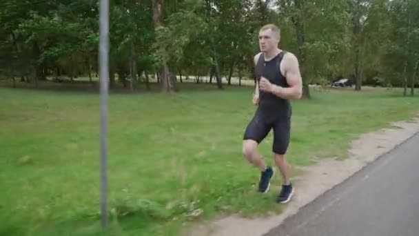 Mañana trote, corredor profesional corre en una carretera, entrenamientos de atletas en un entorno natural, preparación para competiciones de triatlón. — Vídeos de Stock