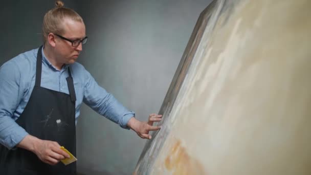 Kunststudio, creatief persoon in blauw hemd en bril aan het werk, een getalenteerde volwassen mannelijke kunstenaar tekent een abstract beeld op een groot doek. — Stockvideo