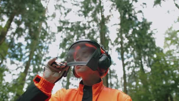Portrét dřevorubce stojícího v lese, specialistky na ochranné oděvy, otevírá hledí ochranné přilby a dívá se do kamery, zpomaluje 4k. — Stock video