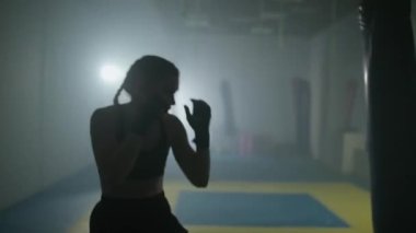 Kadın dövüşçü, boks salonunda yumruk ve savunma antrenmanı yapıyor. Kontür aydınlatma, kadın hızlı saldırıyor..