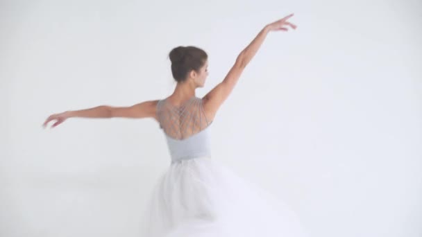 Beyaz etekli zarif bir kadın, bale yapıyor ve beyaz bir arka planda koreografik elementler sergiliyor.. — Stok video