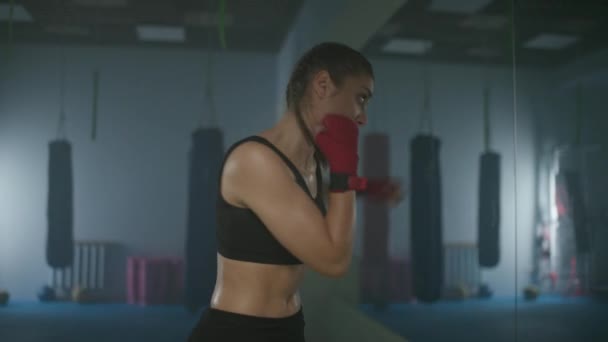 Kadın dövüşçü boks salonunda yumruklarını ve savunmasını eğitiyor, bir boksör aynanın önünde tren kullanıyor, yansımasıyla dövüşüyor, 4k yavaş çekim.. — Stok video