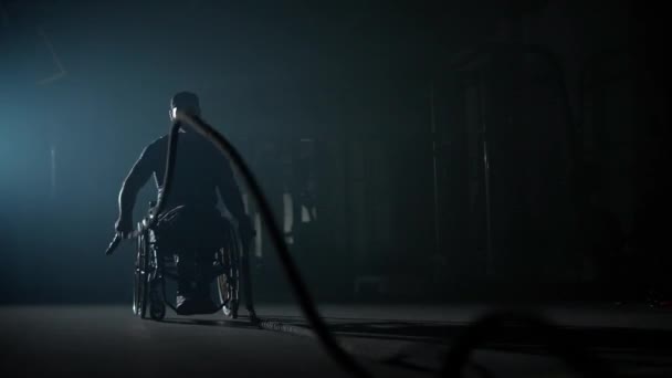 Hombre discapacitado en silla de ruedas, realiza ejercicios con cuerdas de batalla, entrenamiento de resistencia crossfit, entrenamiento de gimnasio y actividad física, 4k cámara lenta. — Vídeos de Stock