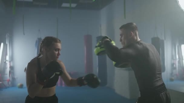 Kadın boksör yumrukları ve savunmayı eğitiyor, odaklanma eldivenlerini yumrukluyor, boks salonunda bir erkek antrenörle antrenman yapıyor, 4k Slow Motion.. — Stok video