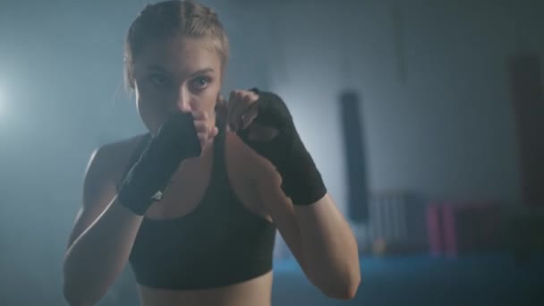 Cámara lenta, luchadora femenina entrena sus golpes, supera un saco de boxeo, día de entrenamiento en el gimnasio de boxeo, cuerpo en forma de fuerza, la chica golpea rápido. — Vídeos de Stock
