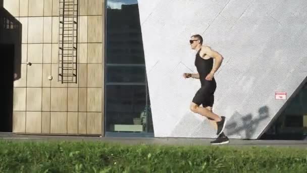 Corredor profesional se ejecuta en una carretera de la ciudad, atleta entrena en un entorno urbano en un día soleado, paisaje urbano moderno, preparación para las competiciones de triatlón. — Vídeos de Stock