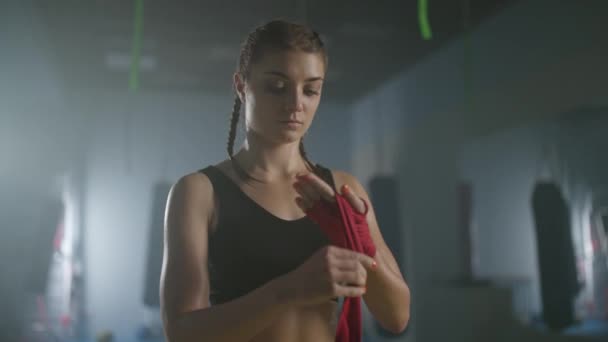 Movimento lento, mulher lutadora envolve suas mãos com bandagens de boxe, dia de treinamento de kickboxing em um ginásio, mulher lutadora está se preparando para a batalha. — Vídeo de Stock