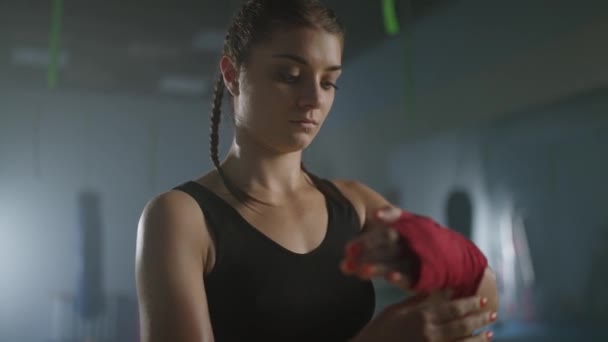Ağır çekimde, kadın boksör ellerini kırmızı boks bandajlarıyla sarar, spor salonunda kickboks antrenmanı yapar, kadın dövüşçü savaşa hazırlanır.. — Stok video