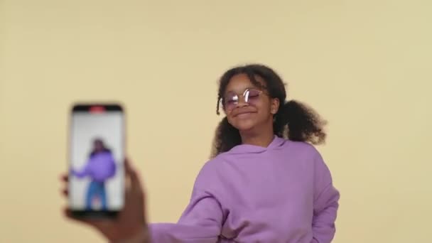 Neşeli Afrikalı kız bej arka planda müzik eşliğinde dans ederken sosyal ağlar için akıllı telefondan video çekiyor.. — Stok video