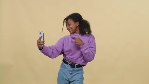 Glada afrikanska kvinnliga danser till musiken på en gul bakgrund och tar en selfie video på smartphone för ett socialt nätverk. — Stockvideo