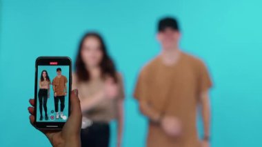 Genç bir adam ve bir kadın, sosyal ağlar için akıllı telefondan video çekerken, akıllı telefon ekranından müzik eşliğinde neşeyle dans ediyorlar..