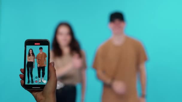 Genç bir adam ve bir kadın, sosyal ağlar için akıllı telefondan video çekerken, akıllı telefon ekranından müzik eşliğinde neşeyle dans ediyorlar.. — Stok video