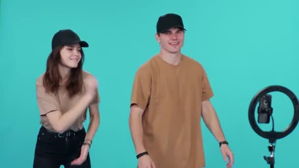Genç çift, sosyal ağlar için akıllı telefondan video çekerken mavi arka planda eş zamanlı olarak müzik eşliğinde dans ediyorlar.. — Stok video