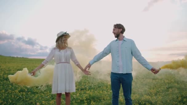Kärlekshistoria, glada par står på fältet våldtäkt hålla händer, man och kvinna hålla gula rökbomber i sina händer, slow motion. — Stockvideo