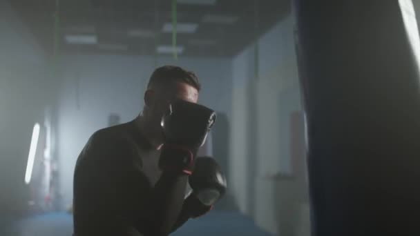 Aggressiv fighter tränar sina slag och försvar i boxning gym, slår en man boxare en slagsäck, 4k slow motion. — Stockvideo